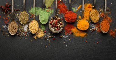 Siyah taş tabakta baharatlı baharat soslu kaşıklar. Doğal baharatların çeşitliliği. Fotokopi alanı olan üst görünüm..