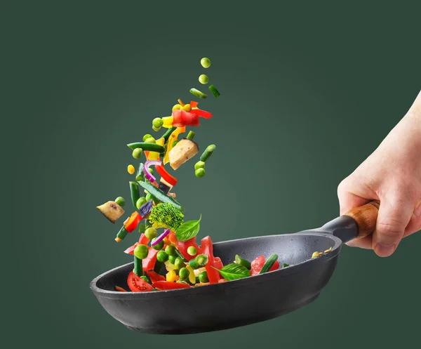 Various chopped vegetables flying into a pan in chef hand on green background