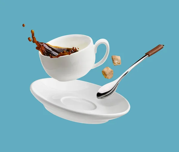 Cup of coffee with a splash drop fly with saucer and spoon isolated on blue