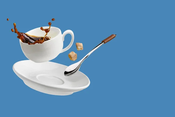 Cup of coffee with a splash drop fly with saucer and spoon isolated on blue with copy space