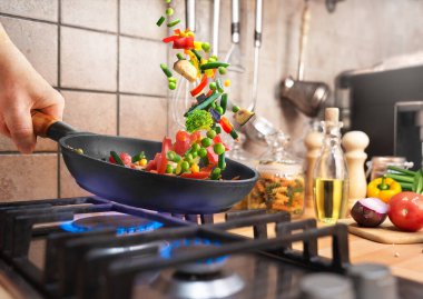 Akşam yemeği için gaz sobasının üstünde tavada sebzeler hazırlıyorum.