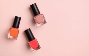 Pembe arka planda mor, mor ve pembe tonlarda üç şişe tırnak cilası. Tam üstte