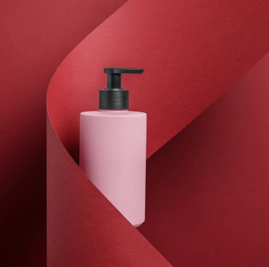 Zengin, koyu kırmızı desenli bir arka plana karşı zarif bir şekilde hazırlanmış modern pembe bir şişe. Güzellik markalaşma kampanyaları için ideal.