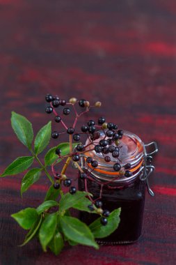 A jar of black elder syrup with fresh elderberries on a wooden table. Herbal medicine.