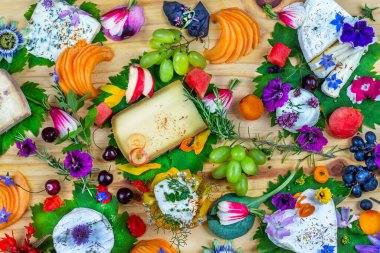 Meyvelerle süslenmiş ve yenilebilir çiçeklerle süslenmiş farklı peynir tabakları.