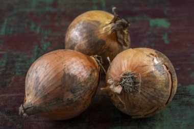 Üç taze soğan, kahverengi derili, kırsal ve dokulu bir masada yatıyor. Soğanlar pürüzsüz ve pürüzsüz yüzeylerin karışımını sergiliyor. Taze görünüşlerini vurguluyorlar..