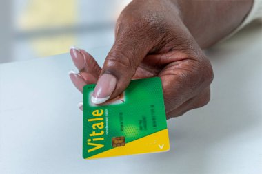 Sarı logolu yeşil bir kimlik kartı tutan biri var. El iyi manikürlü, düzgün cilalanmış tırnaklar sergiliyor. Karta ve el detaylarına odaklan..