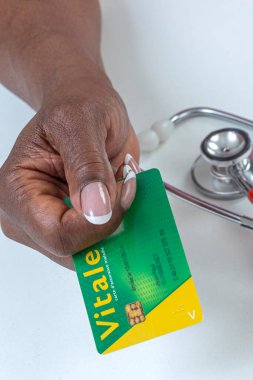 Yeşil ve sarı desenli bir sağlık kartını gösteren bir el steteskopun yanına yerleştirilir. Bu ayar sağlık hizmetleri ve sağlık hizmetlerine odaklanılmasını önerir.