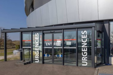 Acil girişinde kalın tabelalı cam kapılar var. Gündüz vakti sağlık merkezinin dışında acil tıbbi yardım arayan hastalara kolay erişim sunar..