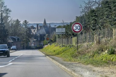 Virajlı bir yol büyüleyici bir kır evine götürür. 30 km 'lik hız limiti işareti görülebiliyor, bu da sakin bir alanı gösteriyor. Yeşillik yemyeşil çizgiler açık gökyüzünün altında yol kenarı.