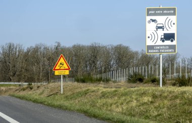 Trafik işaretleri sürücülere otoyol kenarındaki hız kontrolü için sık sık radar kontrolü yapmalarını bildiriyor. Bölge kırsal, arka planda açık bir manzara var..