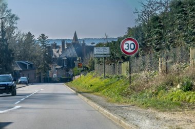 Virajlı bir yol büyüleyici bir kır evine götürür. 30 km 'lik hız limiti işareti görülebiliyor, bu da sakin bir alanı gösteriyor. Yeşillik yemyeşil çizgiler açık gökyüzünün altında yol kenarı.