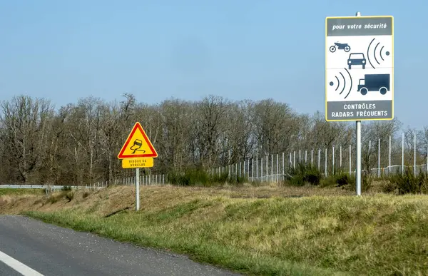 Trafik işaretleri sürücülere otoyol kenarındaki hız kontrolü için sık sık radar kontrolü yapmalarını bildiriyor. Bölge kırsal, arka planda açık bir manzara var..