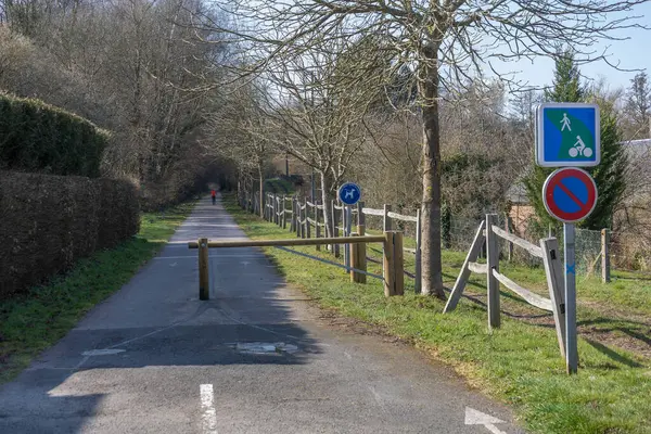 Ağaçlar ve yeşilliklerle çevrili bir bisiklet yolunu engelleyen ahşap bir bariyer. Uzaktan bir yaya görülebiliyor ve işaretler yürüyüş ve bisiklet alanlarını gösteriyor..
