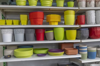 Raflarda düzgünce dizilmiş renkli tencere ve kaplar, farklı boyutlarda ve şekillerde sergileniyor, bahçe ve dekorasyon için uygun. Parlak gölgeler görüntüyü güçlendirir.