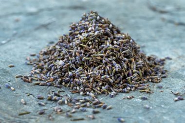 Bir yığın kurumuş lavanta çiçeği desenli taş bir yüzey üzerinde duruyor. Küçük mor tomurcuklar ve gövdeler, doğal güzelliklerini sergileyerek, güzel kokulu ve görsel olarak çekici bir görüntü oluştururlar..