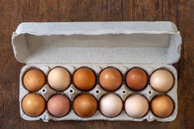 Kırsal bir ahşap yüzeyde gri bir kutuya düzinelerce farklı tonda yumurta yerleştirilir. Yumurtalar kahverengi, benekli ve açık krem tonlarını içerir..