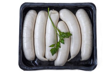 Bir tepside düzgünce dizilmiş birkaç pişmemiş sosis var. Taze yeşil kişniş en üstte duruyor, biraz renk katıyor ve muhtemel baharatı gösteriyor. Arkaplan basit kalıyor, yemekleri vurguluyor..