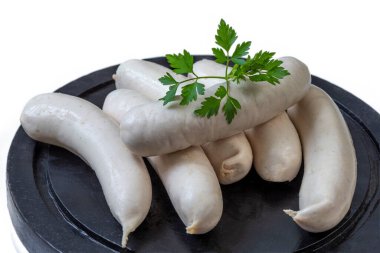 Birkaç beyaz sosis, yeşil kişniş filizi ile süslenmiş siyah bir taş tabakta sunulur. Düzenleme, sosislerin pürüzsüz doku ve şeklini vurgular.