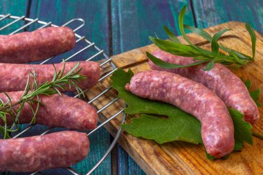 Tahta bir panoda yeşil yapraklar üzerinde dinlenen taze sosisler sergileniyor, otlarla çevrili. Hazırlık, kırsal bir aşçılık tarzını ve canlı renkleri vurguluyor.