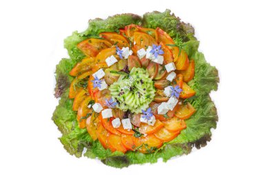 Katmanlı domates, salatalık, salatalık ve otlardan oluşan canlı bir salata, yenilebilir çiçekler ve feta peyniri ile süslenmiş, hepsi kıtır kıtır marul yapraklarıyla çevrili, taze bir yemek için mükemmel..