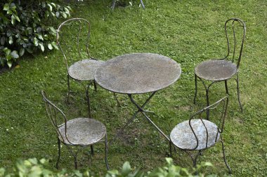 Dört uyumlu sandalyeyle çevrili yıpranmış yuvarlak bir masa canlı yeşil çimenlerin üzerinde oturur. Bu huzurlu bahçe düzenlemesi rahatlamaya ve sosyal toplantılara davetiye çıkarıyor..