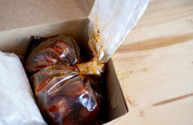 Paketlenmiş beyaz pirinç ve plastik poşetteki sosis siyah biber sosu yatay ahşap masa yüzeyinde izole edilmiş kağıt tabakta çevrimiçi yemek dağıtımı yapıyor..