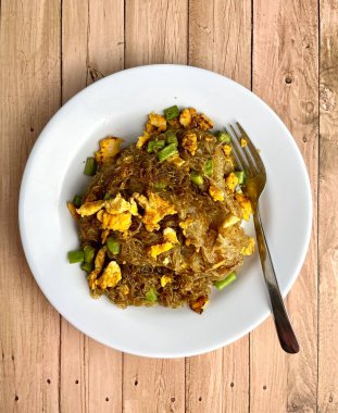 Yağda kızartılmış soya soslu pirinçli şehriye, çırpılmış yumurta ve tabakta uzun fasulye. Yukarıdan bakıldığında, dikey ahşap arka planda yemek fotoğrafçılığı izole edilmiş. Bihun goreng telur.