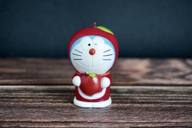 Jakarta, Indonesia - July 3rd, 2024 - Doraemon character with red apple fruit costume. Children or kids toys figure object isolated on dark wooden surface background. clipart