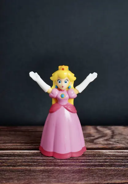 stock image Jakarta, Indonesia - July 3rd, 2024 - Beautiful princess peach from mario cart bros nintendo character. Mcdonalds happy meals toys figure object isolated on dark wooden surface background.