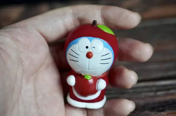 Jakarta, Endonezya - 3 Temmuz 2024 - Kırmızı elma meyvesi kostümlü Doraemon karakteri. Çocuk ya da çocuk oyuncakları koyu ahşap zemin üzerinde izole edilmiş nesne figürleridir..