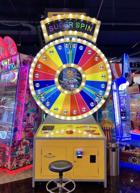 Jakarta, Indonesia - July 18th, 2024 - Arcade yellow and rainbow colored spin wheel toy game machine in game centre  isolated on vertical indoor environment background.