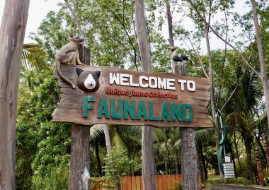 Jakarta, Indonesia - August 6th, 2024 - Faunaland Zoo Ancol logo and wooden sign banner isolated on horizontal outdoor green plants and bright sky background. clipart