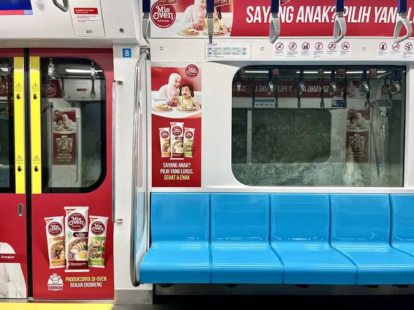 stock image Jakarta, Indonesia - August 9th, 2024 - MRT train vehicle inside interior with empty blue seats and mie oven advertising poster on doors and walls isolated on horizontal ratio background.