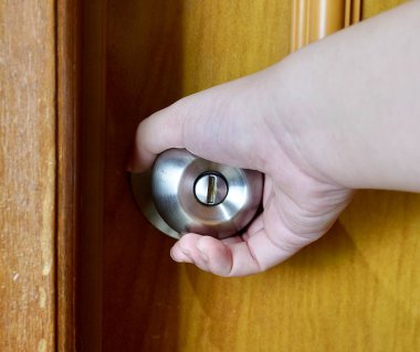 Açık tenli, açık kapı hareketli insan eli yatay kahverengi kapıda izole edilmiş yuvarlak silindir metal banyo kolu arka planında..