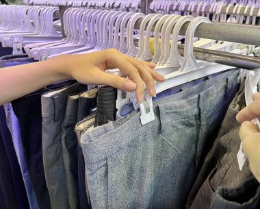 Jakarta, Indonesia - September 1st, 2024 - Customer looking and choosing pants in thrift shop pasar senen store rack. clipart