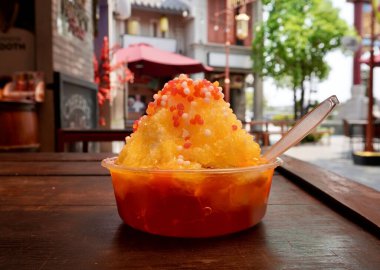 Tatlı mango tıraşlı buzlu tatlı, jöle soslu, yatay oranda izole edilmiş, açık hava yemek salonu ahşap masa arka planında..