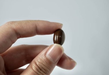 El ele tutuşan koyu kahverengi kapsül hapları sağlık ilaçları ya da yatay beyaz arka planda izole edilmiş vitamin..