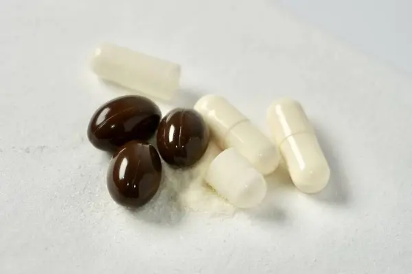 Beyaz kapsül tozu ve yuvarlak koyu kahverengi yağ kapsülü sağlık ilacı veya yatay beyaz arka planda izole edilmiş vitamin..