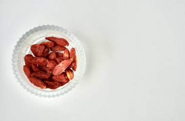 Yuvarlak cam kasedeki kuru kırmızı goji meyvesi ve içecek malzemeleri yatay kopyalanmış beyaz arkaplanda izole edilmiş..