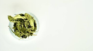 Ezilmiş bitki yaprakları yuvarlak cam kasede yatay kopyada izole edilmiş beyaz arka plan.