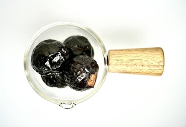 Siyah ya da koyu kahverengi sabun çileği fındıkları ya da beyaz arka planda izole edilmiş ahşap saplı küçük bir fincanda buah lerak..