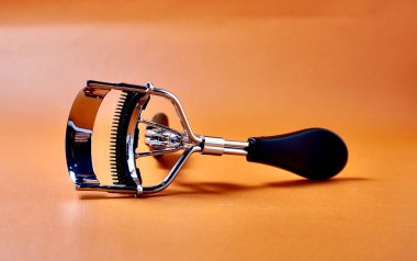 Yatay turuncu kahverengi arkaplanda izole edilmiş metal kirpik bigudi güzellik aracı nesnesi.