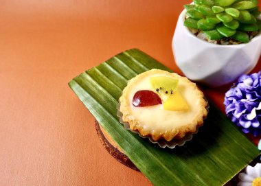 Kue pie vla buah. Kremalı meyveli kek tatlı aperatifi yatay kopyada izole edilmiş turuncu kahverengi terasota arka planında kaktüs ve çiçeklerle süslenmiş..