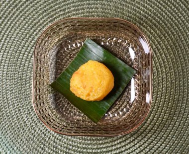 Sarı yuvarlak jadana pasar bika ambon kek dilimi muz yaprağı üzerinde ve şeffaf plaka yatay yeşil plasemat yüzey arkaplan üst açı görünümünden izole.
