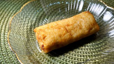 Bir parça kızarmış sosis tek başına atıştırmalık. Yatay yeşil desenli masa örtüsü arka planında izole edilmiş..