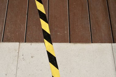 Çizgili sarı çıkartma çizgisi ayırıcısı yatay ahşap panel ve seramik döşeme yüzeyi arka planında izole edildi.