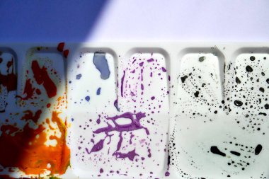 Plastik palette kurumuş turuncu, mor ve gri guaj boyası var. Sanatçı veya boya ekipmanı nesnesi üst açı görünümünden yatay oran arkaplanı izole.