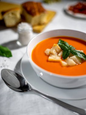Gazpacho with croutons and basil in a white soup bowl served on a white tablecloth.