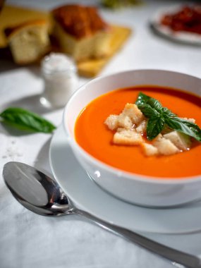 Gazpacho with croutons and basil in a white soup bowl served on a white tablecloth.